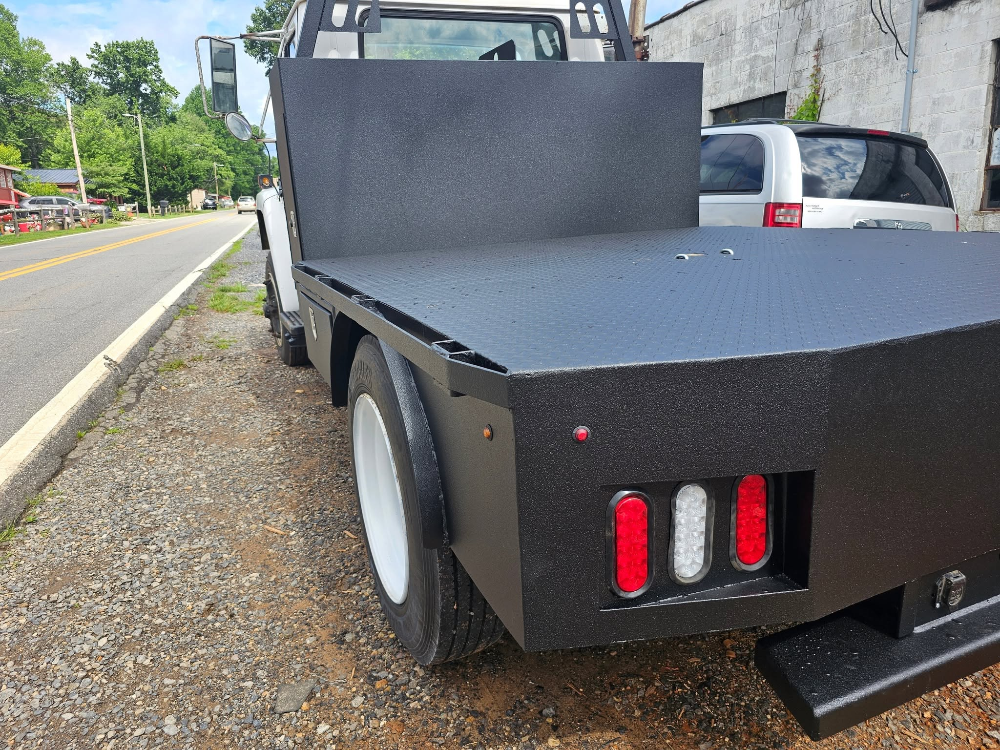 Coated flatbed body on a white work truck outside the shop